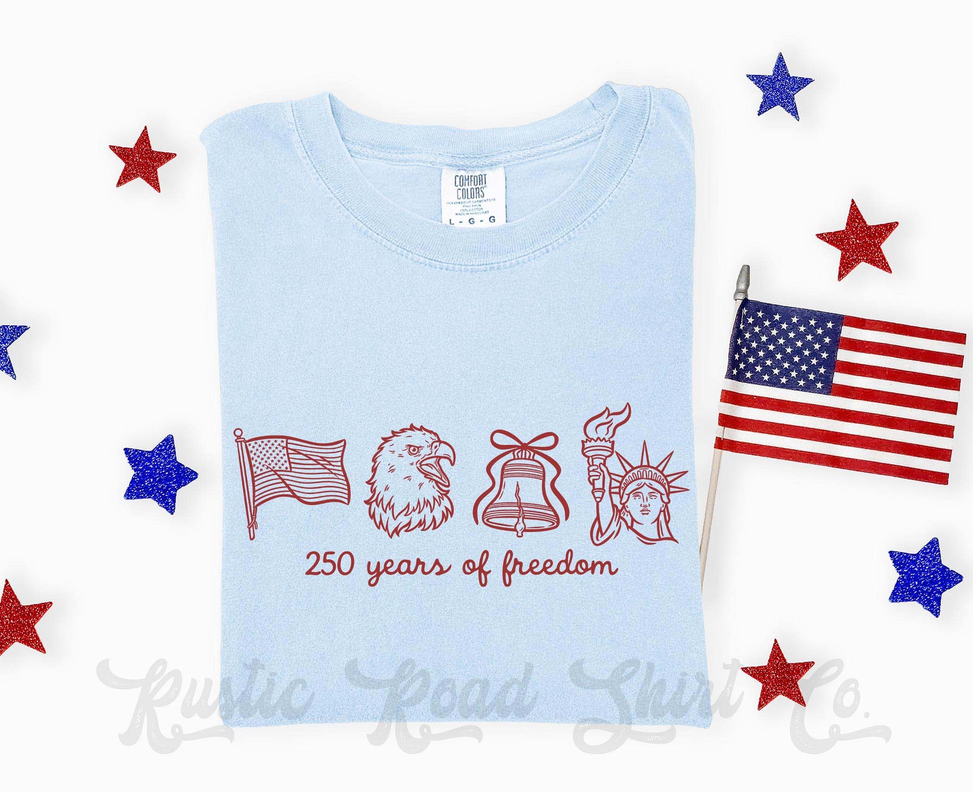 Light blue t-shirt with red graphics and text on a white background with decorative stars and an American flag.