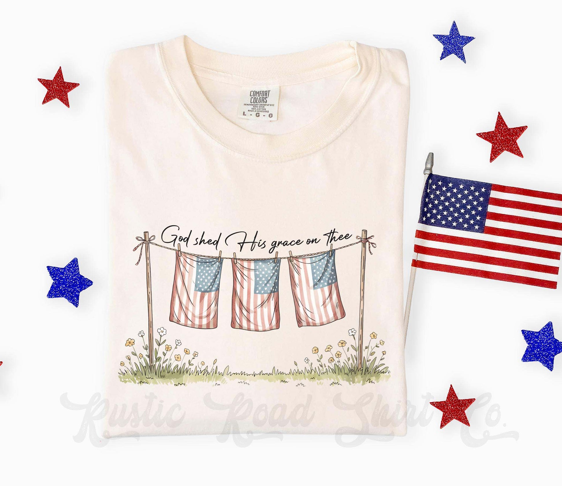 White t-shirt with graphic design of American flags and text, surrounded by decorative stars and an American flag.