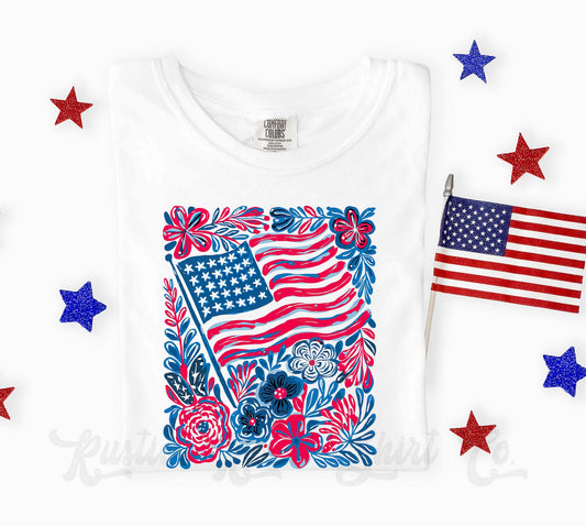 White t-shirt with a floral American flag design on a white background with small American flags and stars.