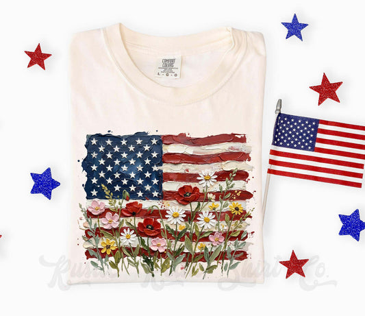 White t-shirt with American flag and floral design, surrounded by decorative stars and a small American flag.