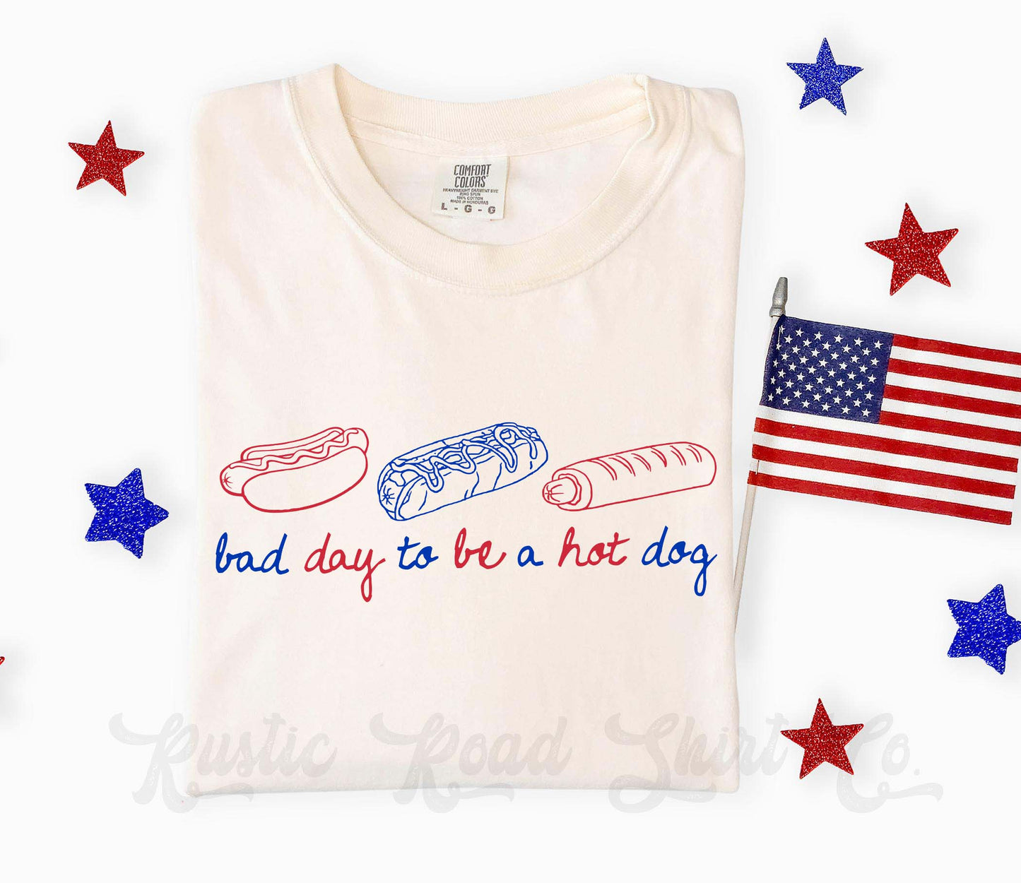 Folded white t-shirt with hot dog, bun, and sausage graphic and text 'bad day to be a hot dog' on a white background with stars and an American flag.