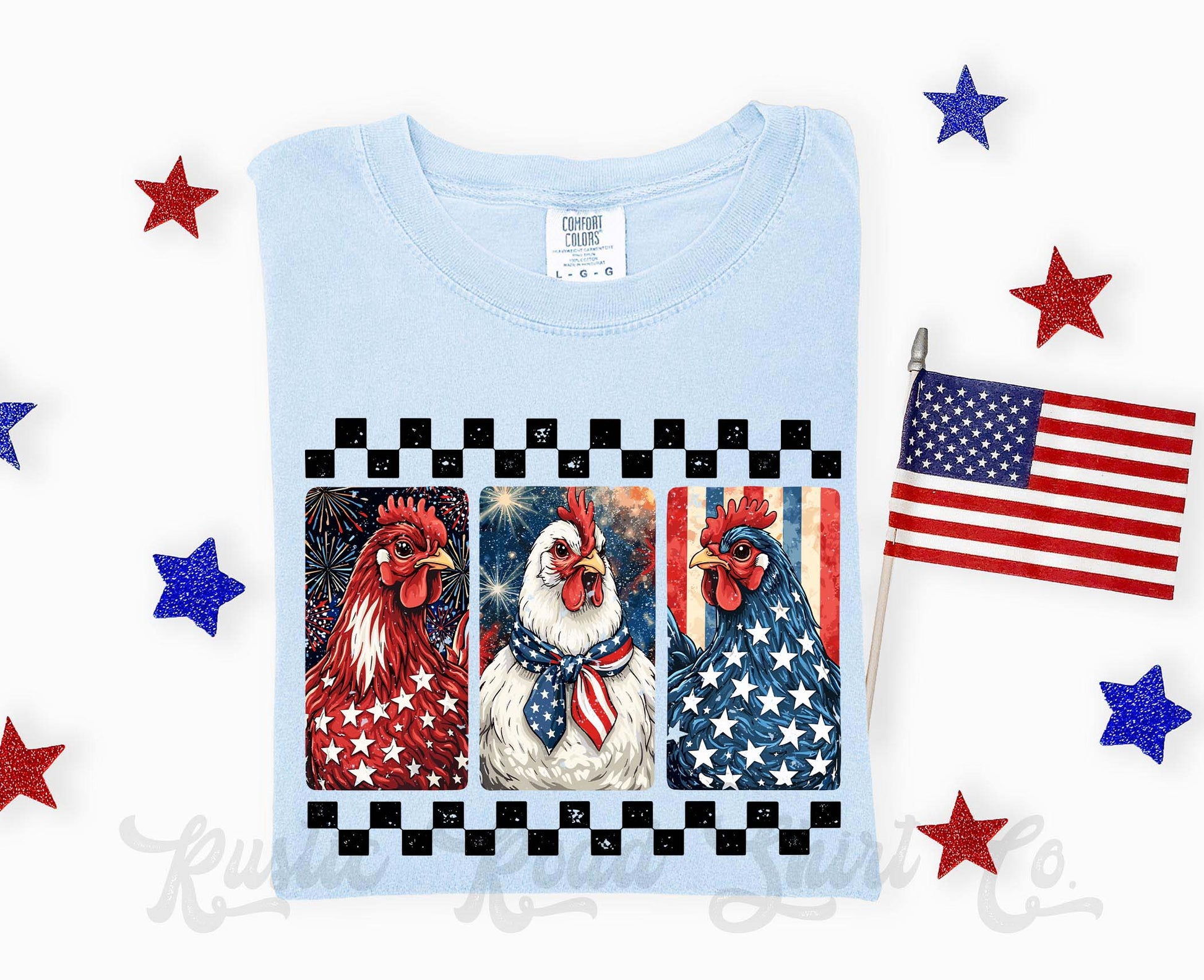 Light blue t-shirt with rooster design featuring American flags and stars, accompanied by a small American flag and decorative stars on a white background.