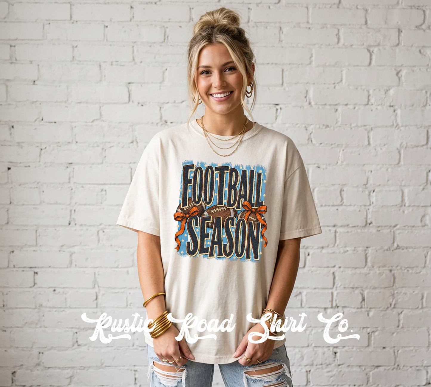 A woman wearing a cream-colored graphic t-shirt with 'FOOTBALL SEASON' printed in blue and orange, standing against a white brick wall. A watermark for 'Krusty Road Shirt Co' is visible at the bottom.