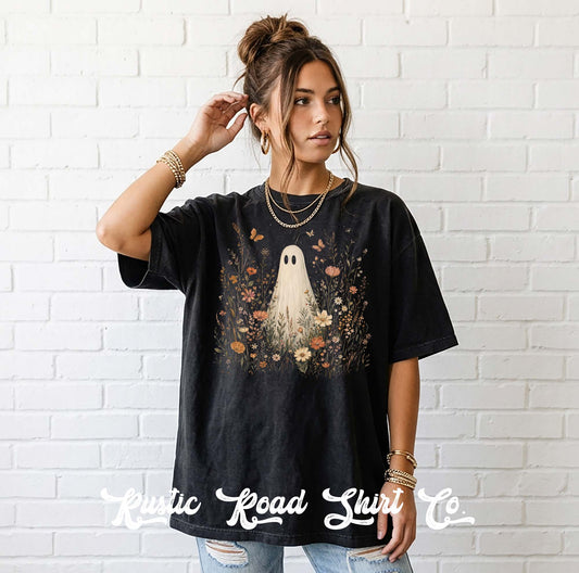 A woman wearing a black graphic t-shirt with a ghost and floral design, standing against a white brick wall. The text 'Rustic Road Shirt Co' is overlaid at the bottom.