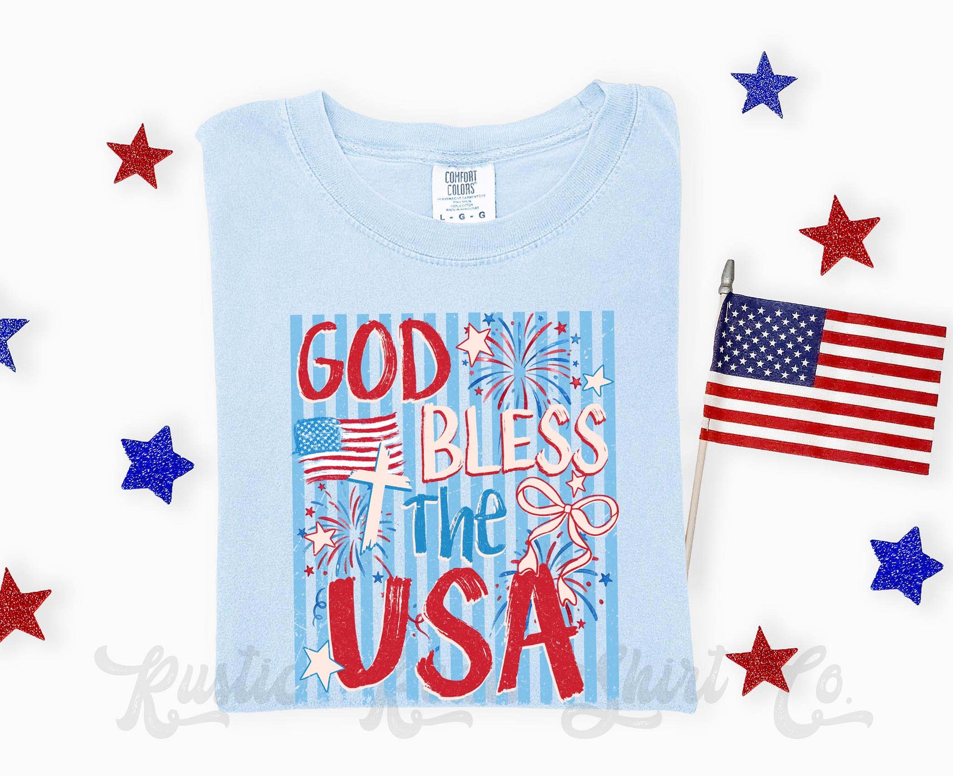 Light blue t-shirt with 'God Bless the USA' text and American flags, surrounded by decorative stars and a small American flag.