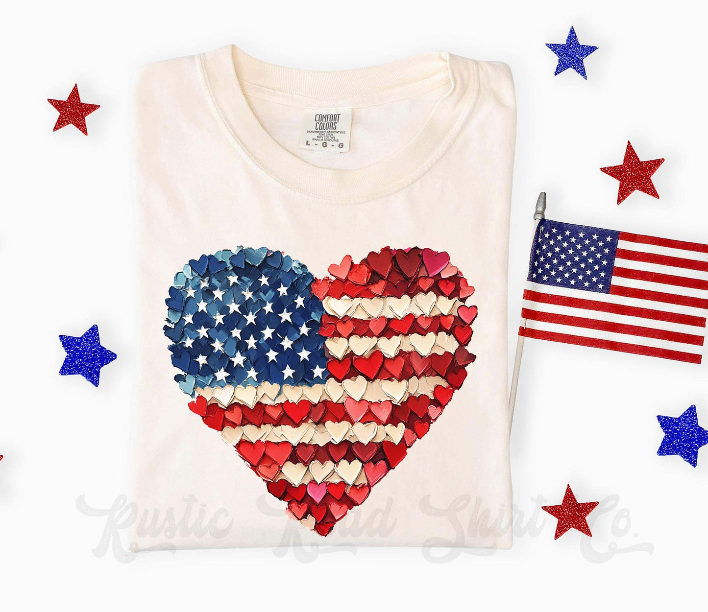 White t-shirt with a heart-shaped American flag design, surrounded by stars and an American flag on a white background.