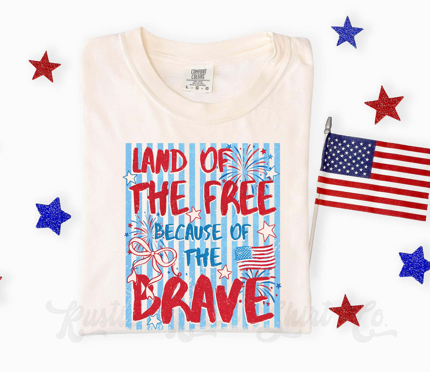 White t-shirt with 'Land of the Free Because of the Brave' text and American flag design, surrounded by stars and a small American flag.
