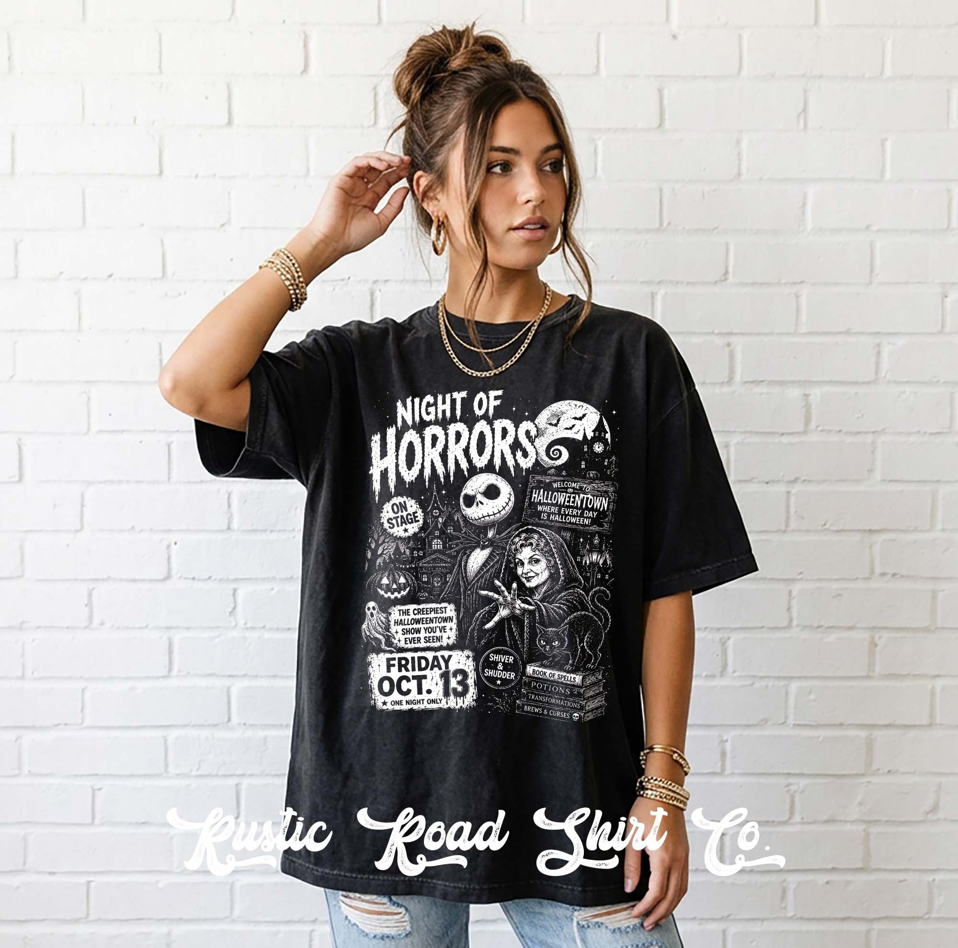 A woman wearing a black graphic t-shirt with a white 'Night of Horrors' print, standing against a white brick wall. The shirt features a detailed horror-themed graphic with a skull, a zombie, and event text.